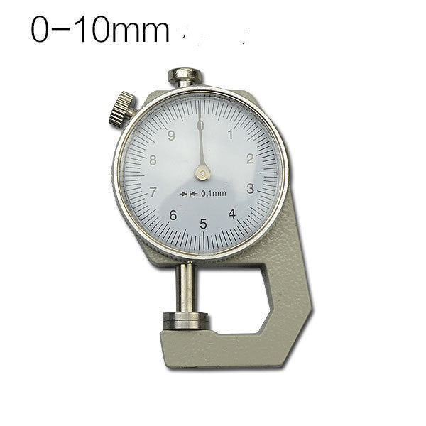 A dial thickness gauge with a silver body and dial, placed on a grey surface, with a yellow box in the background having Chinese characters printed on it.