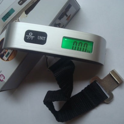 A hand holding a black luggage scale with a green LCD screen displaying weight, featuring a hook and button for operation.