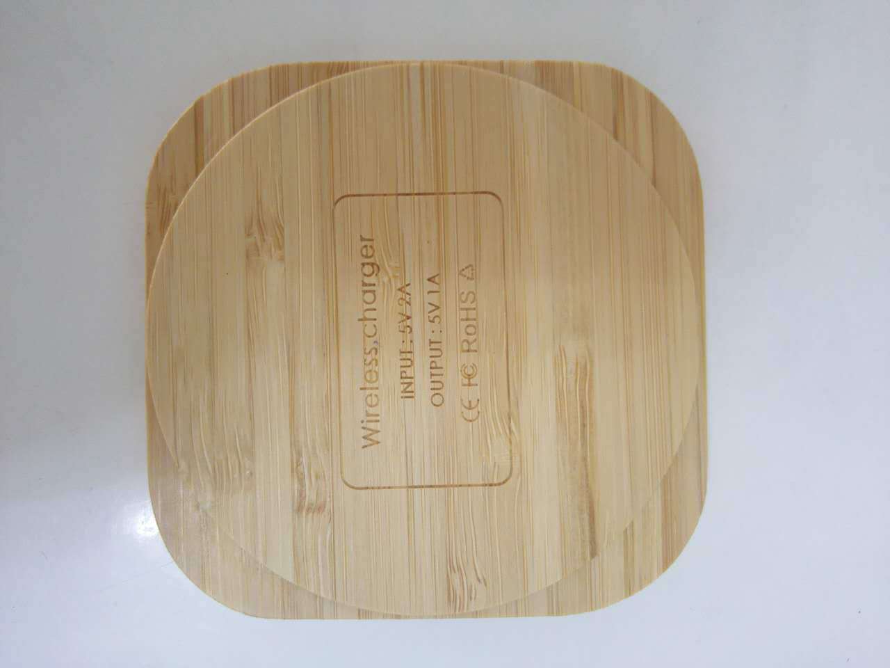 A wooden bamboo wireless charger with a USB port, in a square shape.