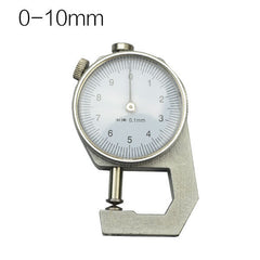 A dial thickness gauge with a silver body and dial, placed on a grey surface, with a yellow box in the background having Chinese characters printed on it.