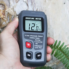 Moisture meter held in a hand with a wooden background