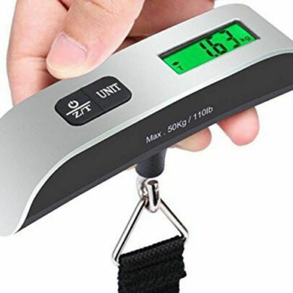 A hand holding a black luggage scale with a green LCD screen displaying weight, featuring a hook and button for operation.