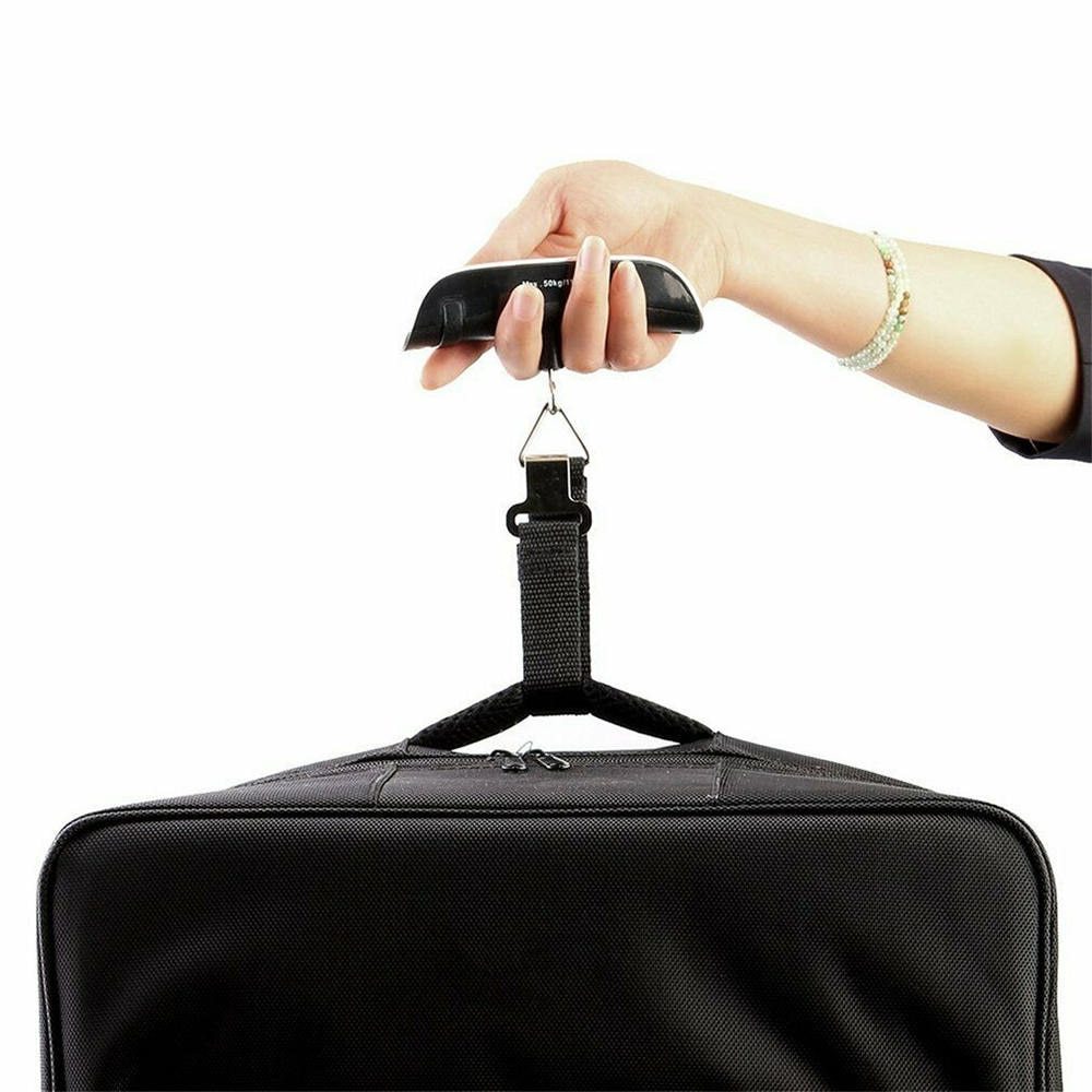 A hand holding a black luggage scale with a green LCD screen displaying weight, featuring a hook and button for operation.