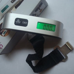 A hand holding a black luggage scale with a green LCD screen displaying weight, featuring a hook and button for operation.