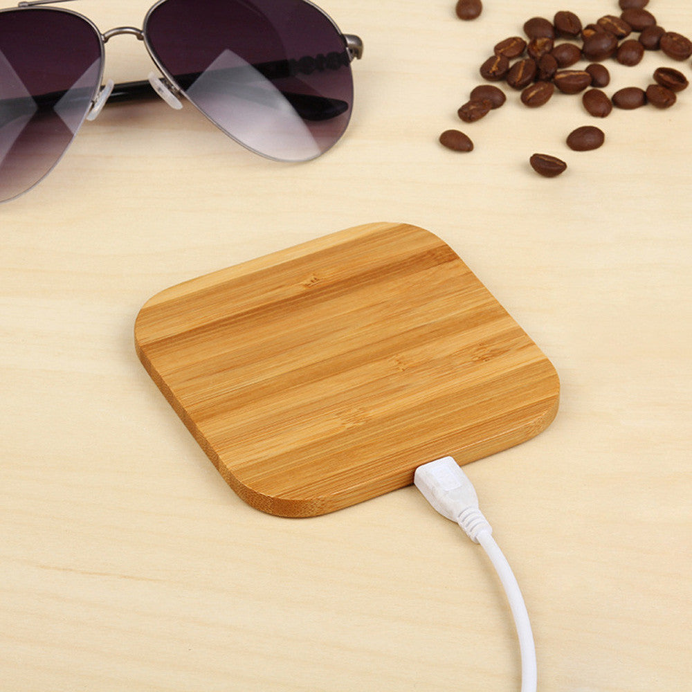 A wooden bamboo wireless charger with a USB port, in a square shape.
